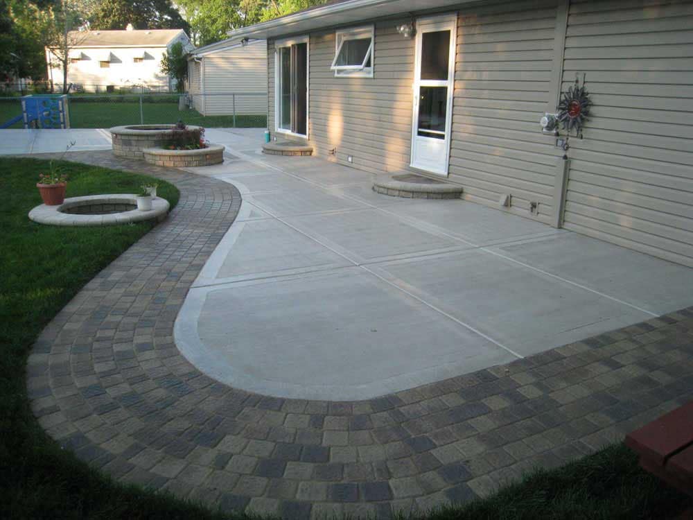 Outdoor concrete patio with decorative brick border and fire pit in residential backyard.