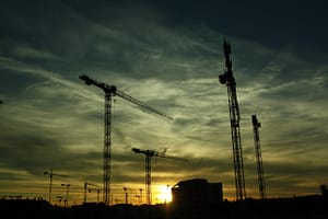 Multiple tower cranes operating at a construction site during sunset