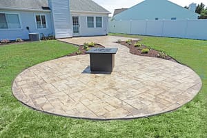 Decorative stamped concrete patio with a central fire pit in a modern backyard.