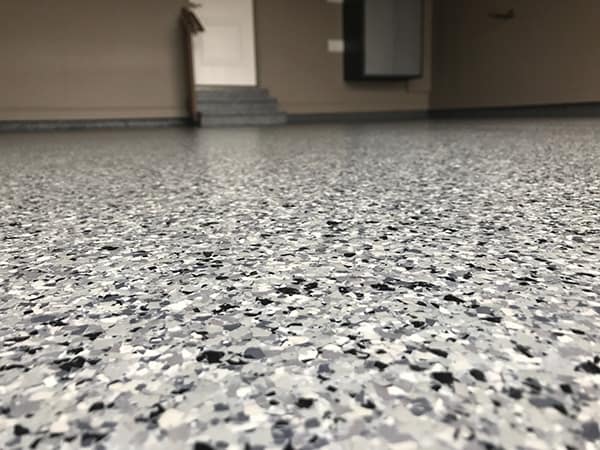 Close-up view of a grey epoxy flake garage floor coating installed in Calgary by Tenmen Construction for durability and style.